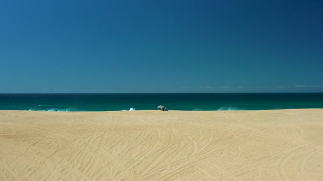 LA LAGUNA BEACH LOS CABOS MEXICO-2021: Waves Rolling Onto Sandy Beach with Distant Umbrella