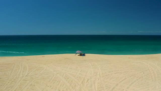 LA LAGUNA BEACH LOS CABOS MEXICO-2021: Beachgoers Relaxing Under Umbrella on Sandy Shore