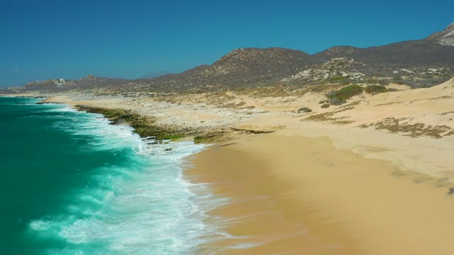 LA LAGUNA BEACH LOS CABOS MEXICO-2021: Waves Rolling Onto Sandy Beach with Rocky Coastline