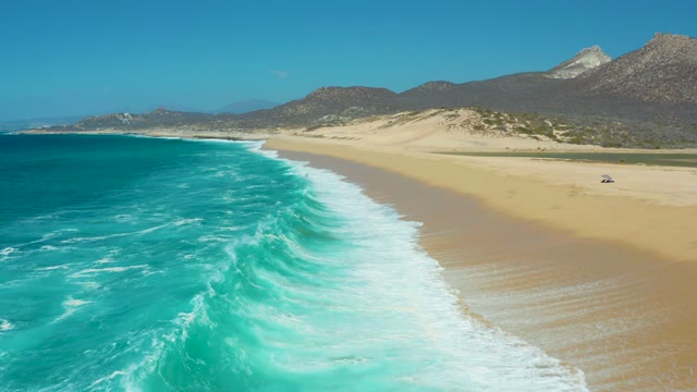 LA LAGUNA BEACH LOS CABOS MEXICO-2021: Waves Rolling Onto Sandy Shore with Distant Mountains