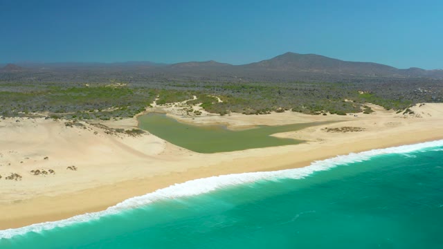 LA LAGUNA BEACH LOS CABOS MEXICO-2021: Gentle Ocean Waves Lapping at Sandy Shore with Lagoon