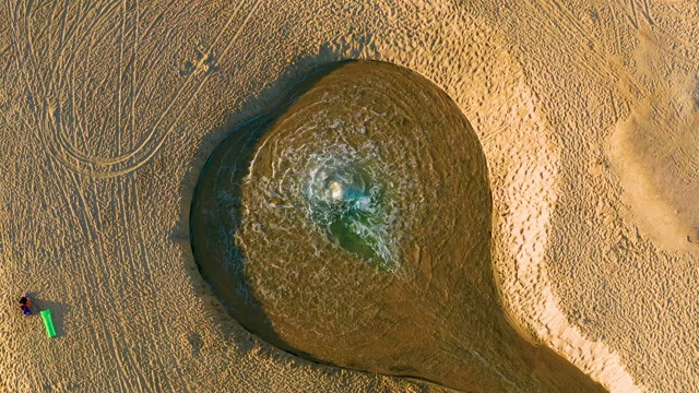 Person with Green Bucket near Muddy Water Pool on Sand