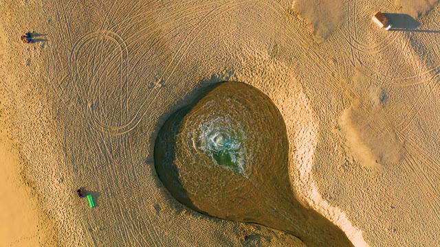 People Moving near Circular Wet Sand Pool on Beach