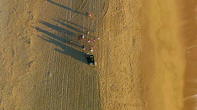 People and Vehicle on Sandy Beach with Advancing Waves