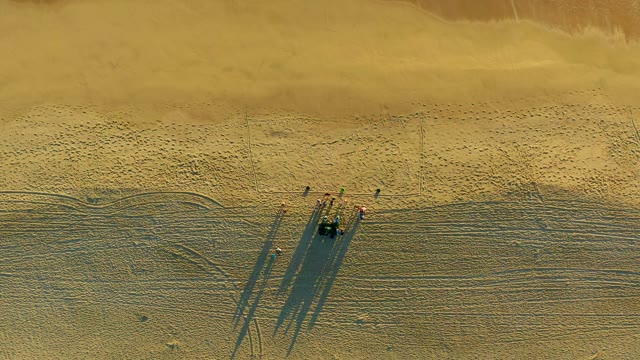 People Walking on a Sandy Beach with Long Shadows