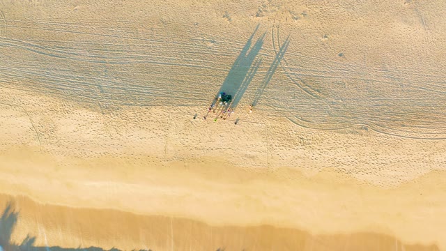 People Walking on Sandy Beach with Long Shadows