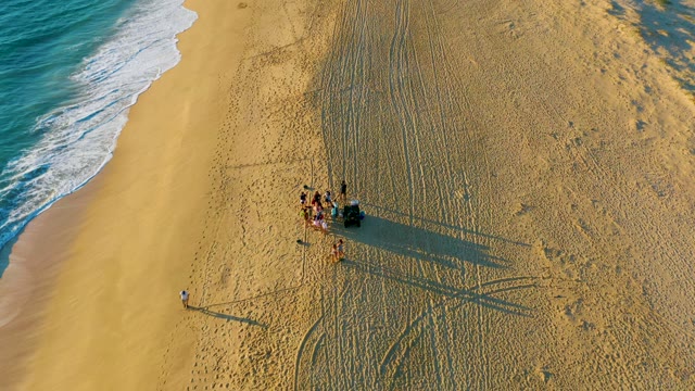 People and Vehicle on Sandy Beach with Ocean Waves