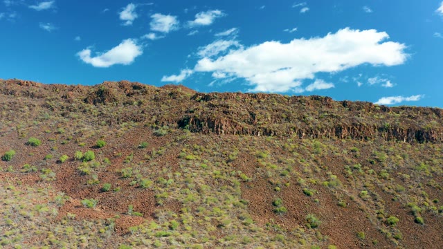 SAN JAVIER BCS MEXICO-2020: Reddish Rocky Slope with Sparse Greenery and Drifting Clouds
