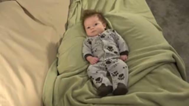 WESTMINSTER COLORADO-2015: Baby Wearing Grey and Black Sleeper Lies on Green Blanket