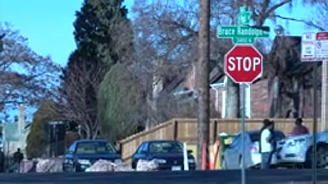 DENVER COLORADO-2015: A Small Group Of People Standing At A Stop Sign In Front Of A Brick Building