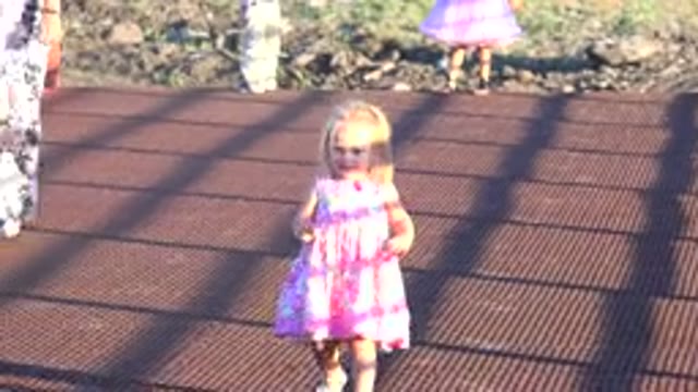 MESA COLORADO-2016: Girl Wearing Pink Dress Walks Across Dark Red Deck On A Sunny Day