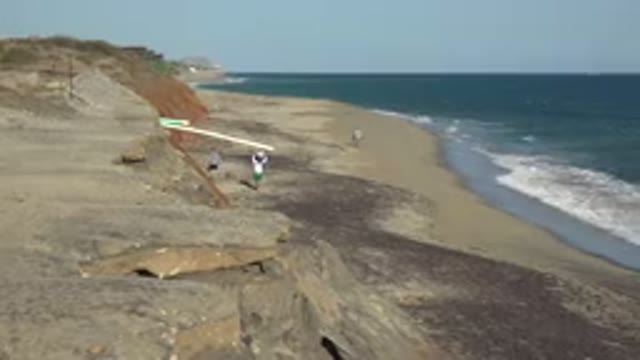 GRAND JUNCTION COLORADO-2017: A Couple Strolls Along a Sandy Beach With Cliffs and Waves