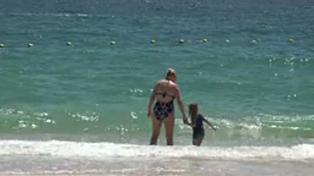 CABO SAN LUCAS MEXICO-2019: Small Ocean Wave Crashes On Mother Holding Daughter's Hand
