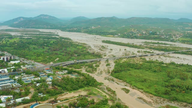 SAN JOSE DEL CABO BCS MEXICO-2021: Flooded River Flowing Past Bridge and Green Landscape