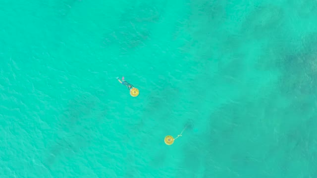 LAGUNA BEACH LOS CABOS BCS MEXICO-2021: Two People Floating on Yellow Rings in Turquoise Water