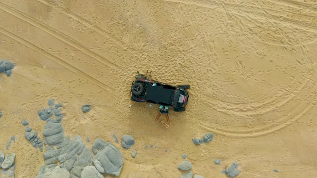 LAGUNA BEACH LOS CABOS BCS MEXICO-2021: People Moving Rocks Near Black SUV in Sandy Terrain