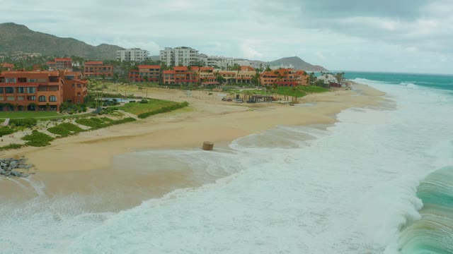 DREAMS RESORT LOS CABOS BCS MEXICO-2021: Ocean Waves Advancing on Sandy Shore with Coastal Buildings