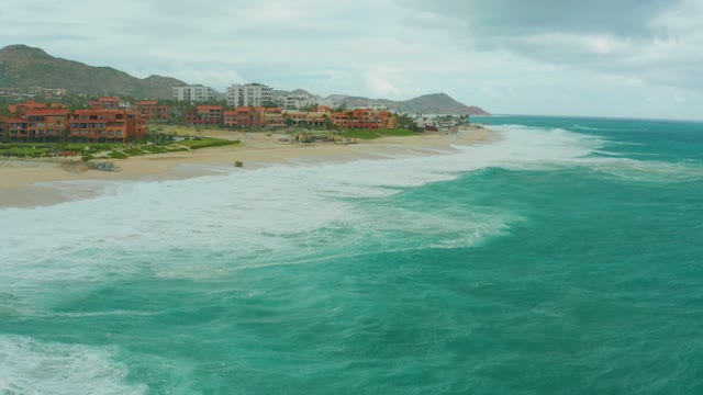 DREAMS RESORT LOS CABOS BCS MEXICO-2021: Waves Crashing Onto Sandy Beach with Coastal Buildings