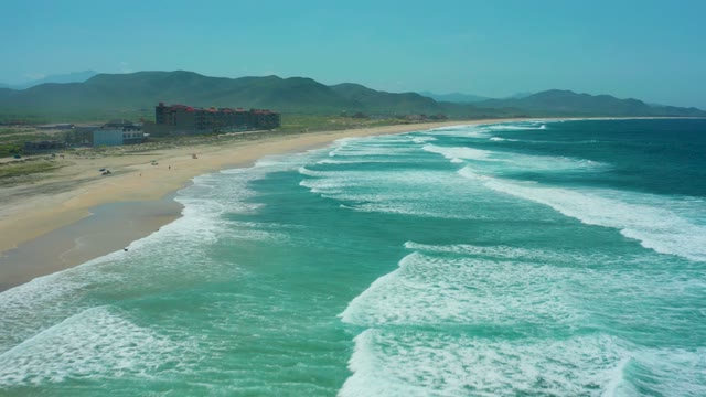 CERRITOS BEACH BCS MEXICO-2021: Waves Crashing on Sandy Shore with Distant Buildings