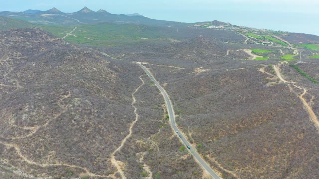 LA PLAYITA LOS CABOS MEXICO-2021: Winding Road with Moving Vehicle in Hilly Landscape