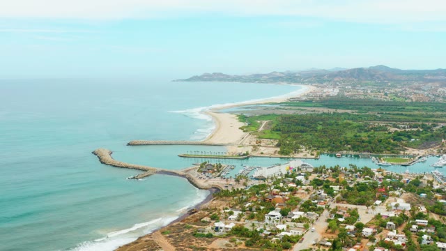 LA PLAYITA LOS CABOS MEXICO-2021: Waves Rolling Onto Sandy Beach with Harbor and Town