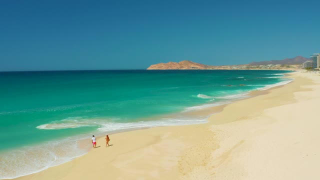 DREAMS LOS CABOS BCS MEXICO-2021: Two People Strolling on a Sandy Beach by Turquoise Waters