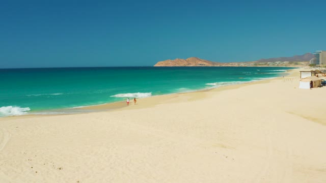 DREAMS LOS CABOS BCS MEXICO-2021: People Walking Along Sandy Beach with Turquoise Ocean Waves