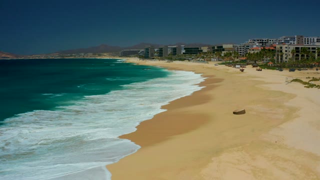 DREAMS LOS CABOS BCS MEXICO-2021: Waves Rolling Onto Sandy Beach with Distant Buildings