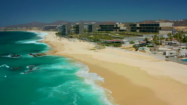 DREAMS LOS CABOS BCS MEXICO-2021: Waves Rolling Onto Sandy Shore with Coastal Buildings