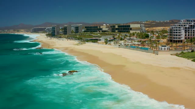 DREAMS LOS CABOS BCS MEXICO-2021: Gentle Ocean Waves Rolling Onto Sandy Shore with Coastal Buildings