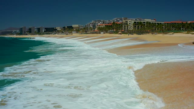 DREAMS LOS CABOS BCS MEXICO-2021: Waves Crashing Onto Sandy Shore with Coastal Buildings