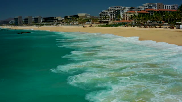 DREAMS LOS CABOS BCS MEXICO-2021: Waves Rolling Onto Sandy Shore with Coastal Buildings