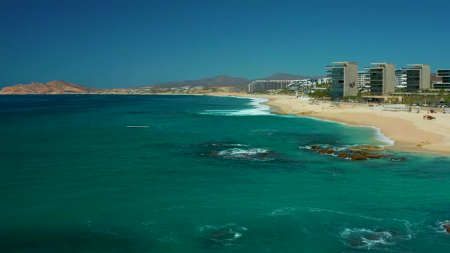 DREAMS LOS CABOS BCS MEXICO-2021: Waves Rolling Onto Sandy Shore with Coastal Buildings