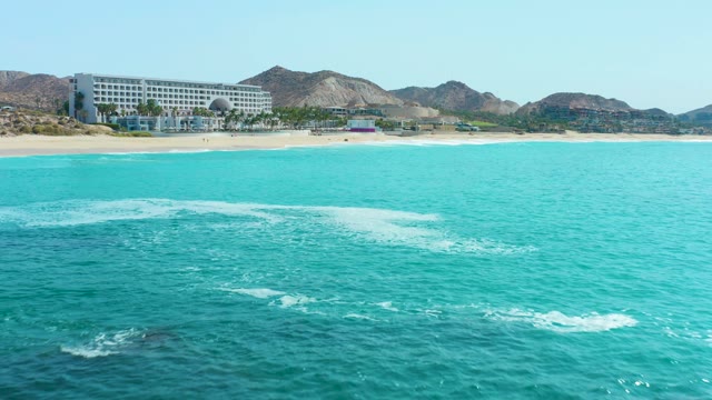 MARQUIS LOS CABOS MEXICO-2021: Ocean Waves Rolling Toward Sandy Beach with Coastal Building