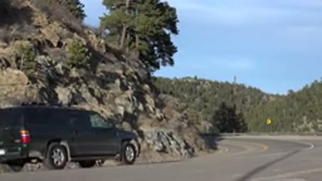 NEDERLAND COLORADO-2015: Several Cars Turn Left On A Road With Mountains Covered