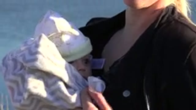 WESTMINSTER COLORADO-2015: Woman Wearing Brown Jacket Holds Baby Wrapped In Gray