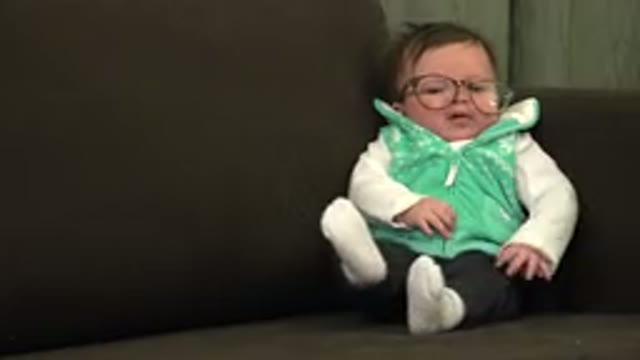 WESTMINSTER COLORADO-2015: Baby Wearing Green Vest With Glasses Sits On Brown Sofa
