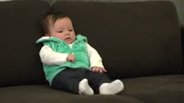 WESTMINSTER COLORADO-2015: Baby Wearing Green Vest Sits On Brown Sofa Looking At Camera