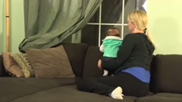 WESTMINSTER COLORADO-2015: Woman Wearing Blue Shirt Sits On Brown Sofa Holding Baby