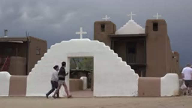 TAOS NEW MEXICO-2015: Two Friends Slowly Strolling Past The Big White Church