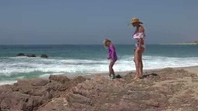 CABO SAN LUCAS MEXICO-2019: A Woman And A Young Girl In Beach Clothing Are Walking On Rocky Shore