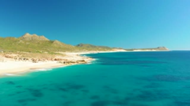 BUZZARDS EAST CAPE LOS CABOS BCS MEXICO-2022: Gentle Ocean Waves on Sandy Beach with Rocky Shores