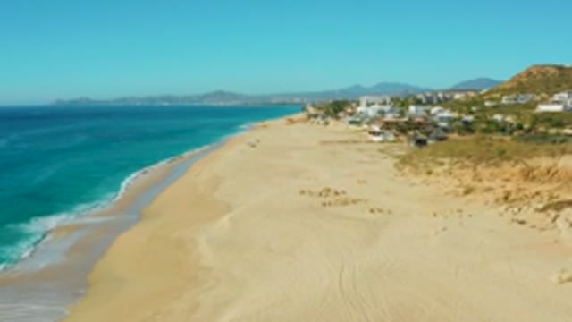 BUZZARDS EAST CAPE LOS CABOS BCS MEXICO-2022: Gentle Waves Lapping a Sandy Beach with Coastal Buildings