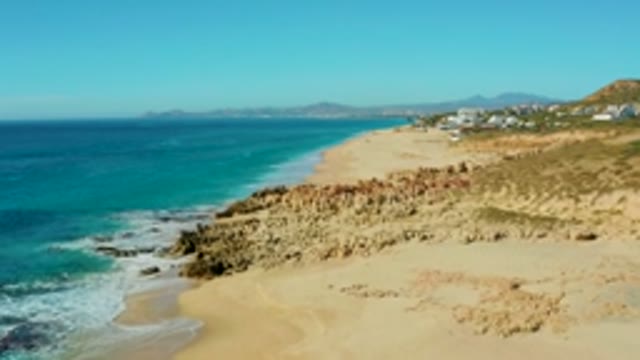 BUZZARDS EAST CAPE LOS CABOS BCS MEXICO-2022: Waves Receding on Sandy Beach with Rocky Cliffs