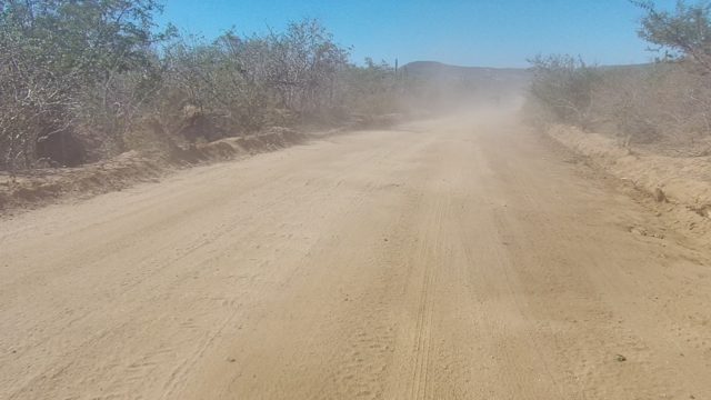 LOS CABOS BCS MEXICO-2022: Dusty Dirt Road with Vehicle Moving Away in Arid Terrain