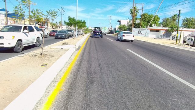 LOS CABOS BCS MEXICO-2022: Car Driving Along Urban Road with Parked Vehicles and Buildings