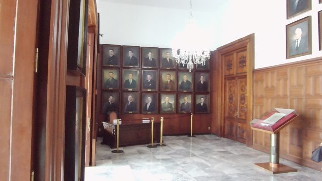 People Moving in a Room with Historical Portraits