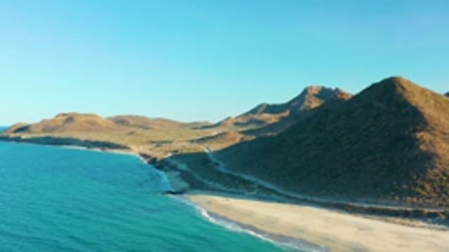 LAS BARRACAS EAST CAPE BCS MEXICO-2022: Gentle Ocean Waves Lapping Sandy Beach by Rocky Hills
