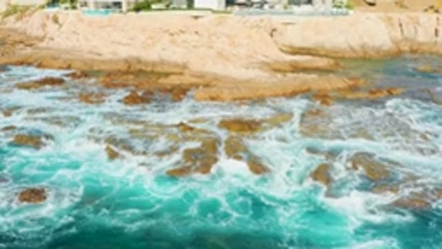 CHILENO BEACH LOS CABOS BCS MEXICO-2022: Waves Crashing on Rocky Shore with Cliffside Buildings