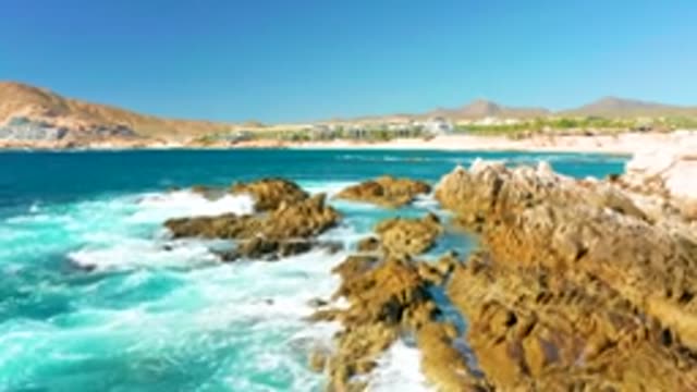 CHILENO BEACH LOS CABOS BCS MEXICO-2022: Waves Crashing on Rocky Shore with Distant Beach